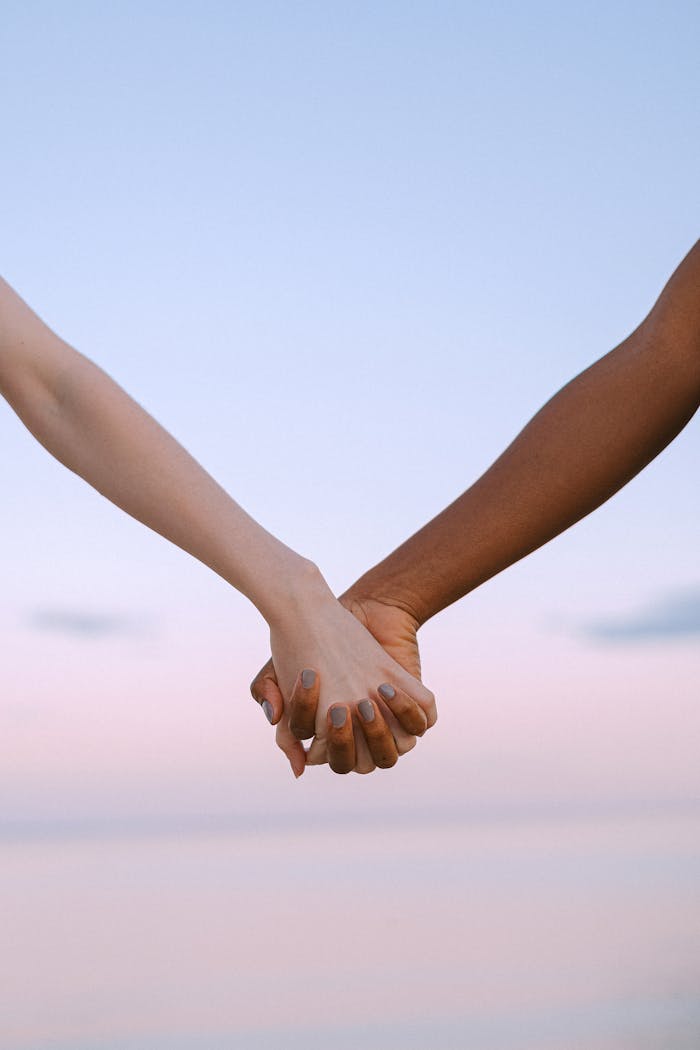 Closeup of multiracial hands holding, symbolizing unity and equality against a serene sky.